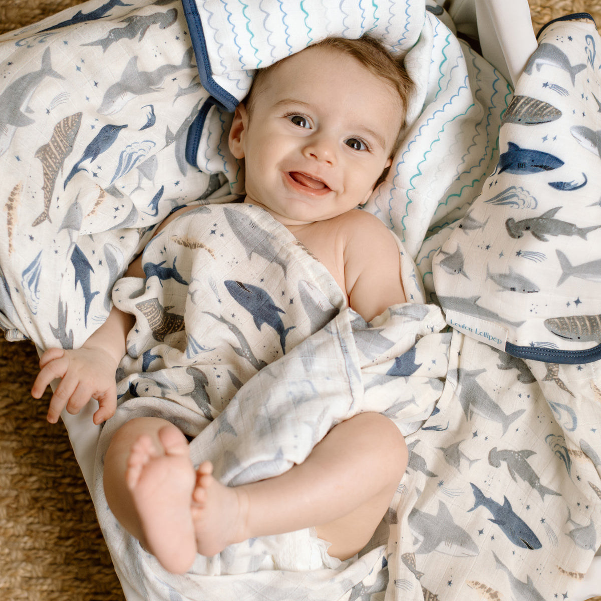 Baby wrapped in a blanket with shark pattern, lying on a soft surface