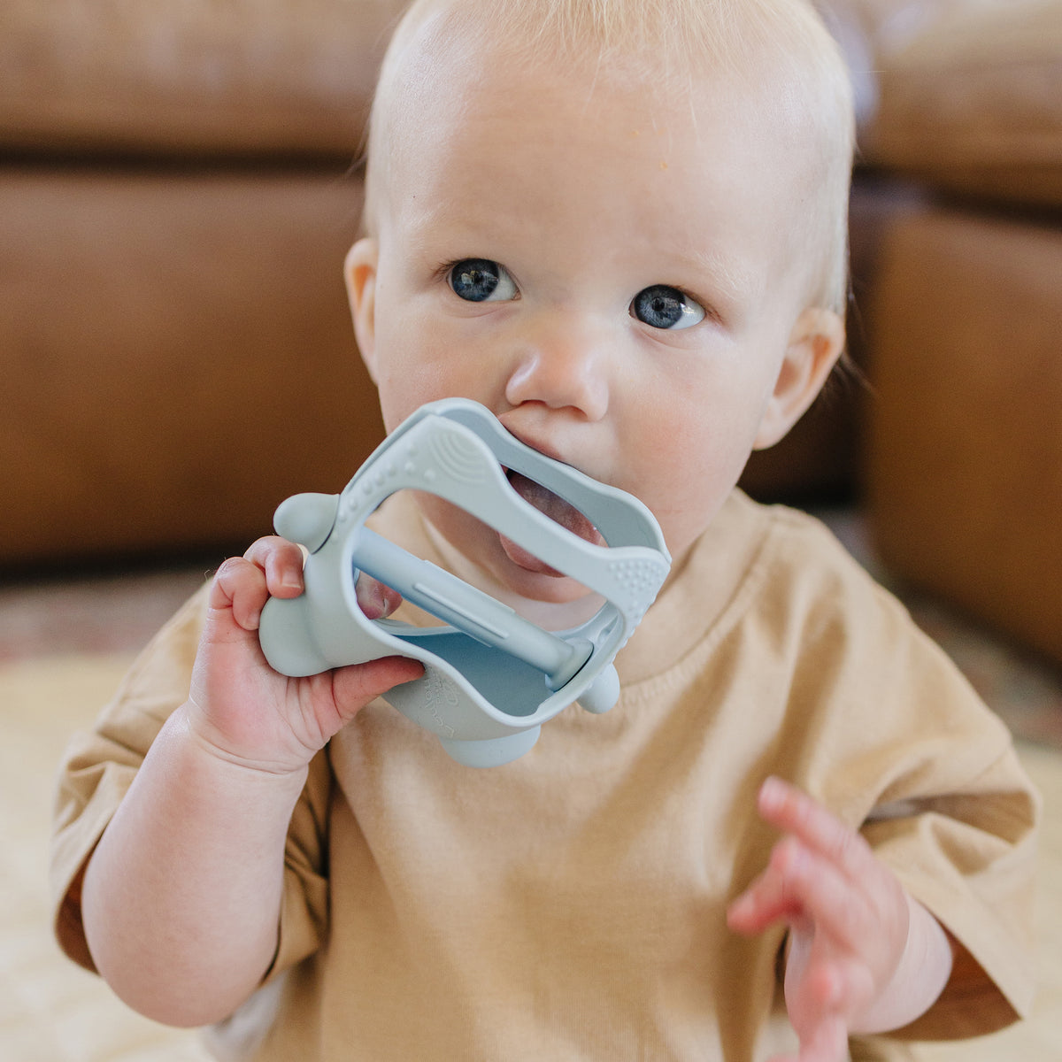Baby holding a blue shark shaped teething mitt indoors