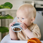 Baby holding a shark shaped teething mitt in a kitchen setting