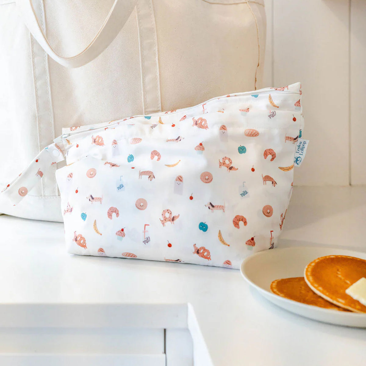 French breakfast patterned wet dry fabric bag on a white surface with pancakes and butter in the background