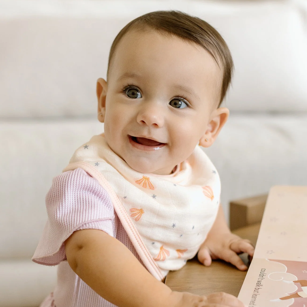 Baby wearing a bib with a smile, sitting on a couch.