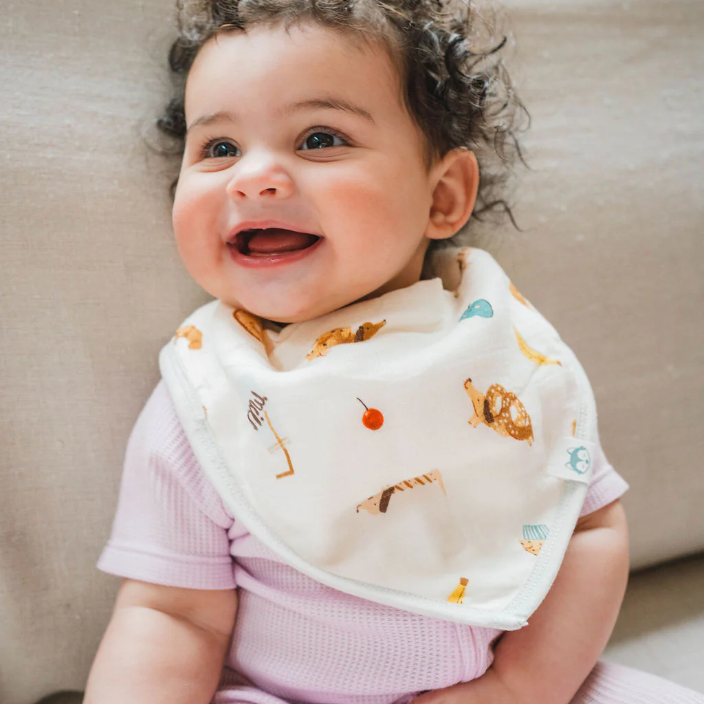 Baby wearing a bib with animal prints, sitting on a beige couch.