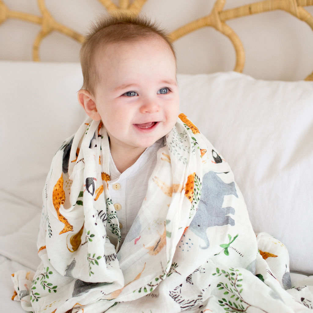 Baby wrapped in a blanket with animal patterns, sitting on a white couch.